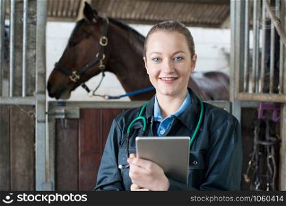 Portrait Of Female Vet With Digital Tablet Examining Horse In Stable