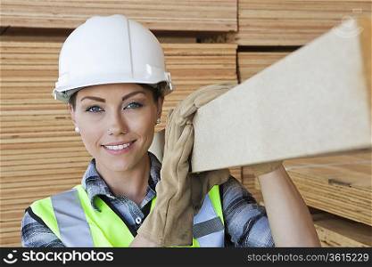 Portrait of female worker carrying wooden plank on shoulder