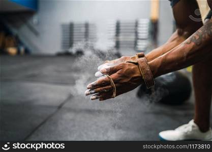 Portrait of fitness young man rubbing hands with chalk magnesium powder, preparing for workout in crossfit gym. Sport and healthy lifestyle concept.