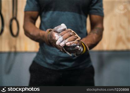 Portrait of fitness young man rubbing hands with chalk magnesium powder, preparing for workout in crossfit gym.
