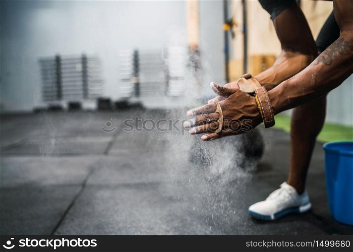Portrait of fitness young man rubbing hands with chalk magnesium powder, preparing for workout in crossfit gym. Sport and healthy lifestyle concept.