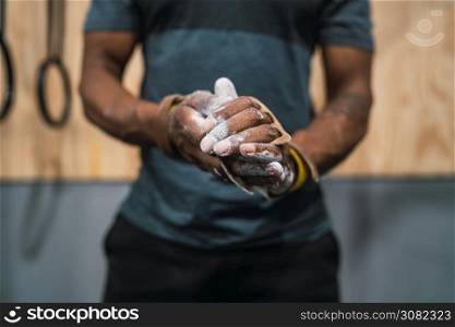 Portrait of fitness young man rubbing hands with chalk magnesium powder, preparing for workout in crossfit gym.