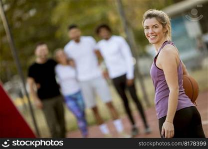 Portrait of fitness young woman with basketball ball playing game outdoor with friends