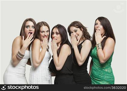 Portrait of five shocked young women with hands over mouth against gray background
