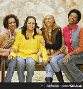 Portrait of four female friends sitting on a bench and smiling