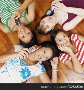Portrait of four young women lying on a hardwood floor and holding mobile phones