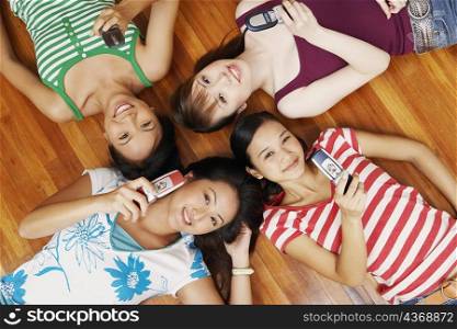Portrait of four young women lying on a hardwood floor and holding mobile phones