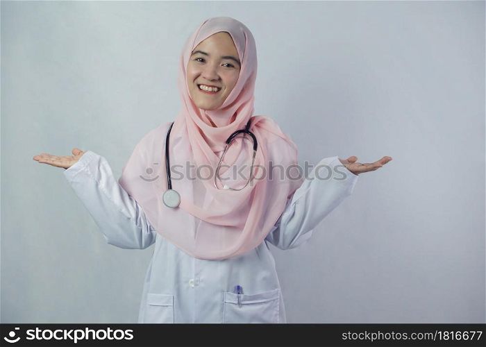 Portrait of friendly, smiling confident Muslim female doctor in hijab dress holding a stethoscope on white background. She looking at camera and stretching both arms out to the side of the body
