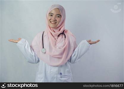 Portrait of friendly, smiling confident Muslim female doctor in hijab dress holding a stethoscope on white background. She looking at camera and stretching both arms out to the side of the body