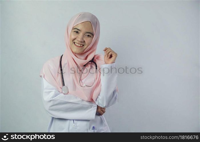 Portrait of friendly, smiling confident Muslim woman doctor in hijab dress holding a stethoscope and looking at camera on white background