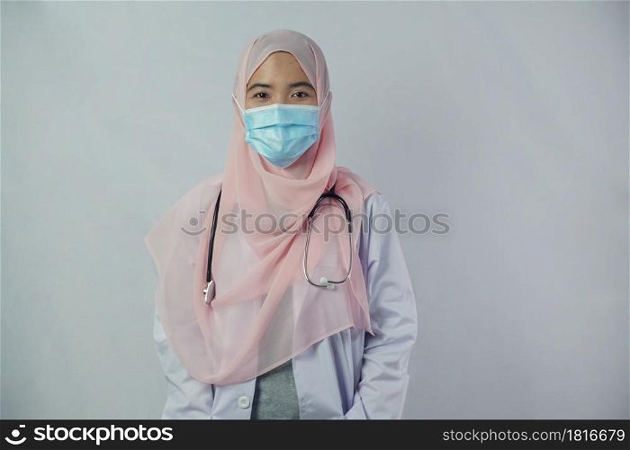 Portrait of friendly, smiling confident Muslim woman doctor in hijab dress wear mask holding a stethoscope and looking at camera on white background
