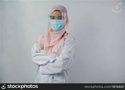 Portrait of friendly, smiling confident Muslim woman doctor in hijab dress wear mask and face shield holding a stethoscope and looking at camera on white background
