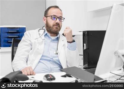 Portrait of friendly smiling healthcare professional therapist sitting at workplace. Happy confident male doctor physician wearing white medical coat and stethoscope. High quality photo. Portrait of friendly smiling healthcare professional therapist sitting at workplace. Happy confident male doctor physician wearing white medical coat and stethoscope.