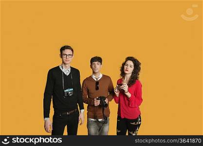 Portrait of friends standing together with cameras over colored background