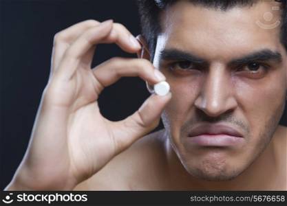 Portrait of frustrated drug addict holding pill against black background