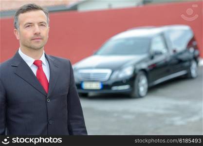 Portrait of funeral director standing in front of hearse