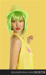 Portrait of funky young woman with green hair puckering her lips against yellow background