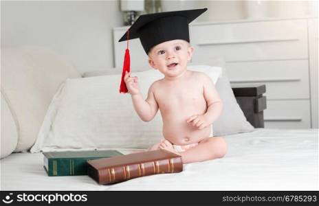 Portrait of funny baby boy in diapers wearing black graduation cap