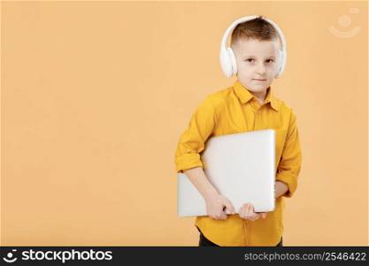 Portrait of funny clever school boy with headphones and laptop in yellow shirt. Yellow studio background. Education. Looking at camera. High quality photo.. Portrait of funny clever school boy with headphones and laptop in yellow shirt. Yellow studio background. Education. Looking at camera. High quality photo