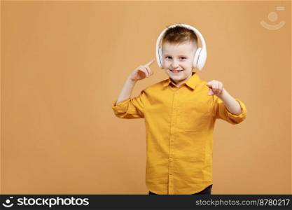 Portrait of funny clever school boy with headphones in yellow shirt. Yellow studio background. Education. Looking, smiling and shows a thumb up at camera. High quality photo.. Portrait of funny clever school boy with headphones in yellow shirt. Yellow studio background. Education. Looking, smiling and shows a thumb up at camera. High quality photo