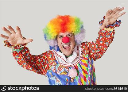 Portrait of funny clown with arms raised and mouth open against colored background