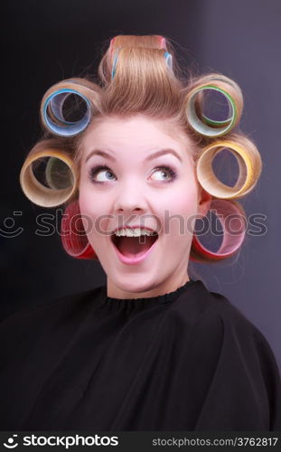 Portrait of funny happy woman in beauty salon. Cheerful blond girl with hair curlers rollers by hairdresser. Hairstyle.