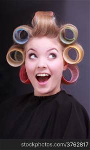 Portrait of funny happy woman in beauty salon. Cheerful blond girl with hair curlers rollers by hairdresser. Hairstyle.