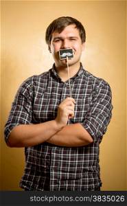 Portrait of funny man holding fake mustache on stick at mouth