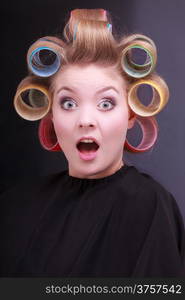 Portrait of funny surprised woman in beauty salon. Shocked blond girl with hair curlers rollers by hairdresser. Hairstyle.