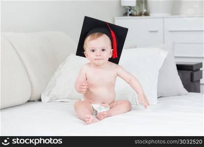 Portrait of funny toddler boy in graduation cap sitting on bed. Portrait of toddler boy in graduation cap sitting on bed