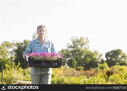 Portrait of gardener carrying crate with flower pots in garden