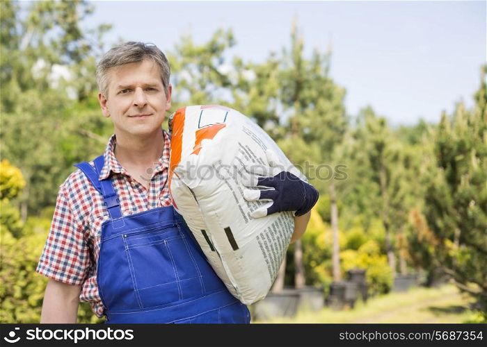 Portrait of gardener carrying sack in plant nursery