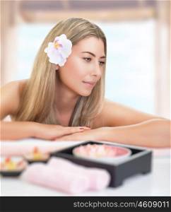 Portrait of gentle blond female with orchid flower in hair lying down on massage table, enjoying beauty treatment in luxury spa salon