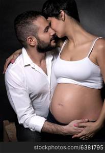 Portrait of gentle romantic couple awaiting baby over black background, happy pregnant woman with husband posing in the studio