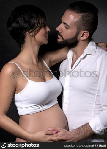 Portrait of gentle romantic couple with love looking on each other over black background, happy pregnant woman with husband posing in the studio
