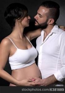 Portrait of gentle romantic couple with love looking on each other over black background, happy pregnant woman with husband posing in the studio