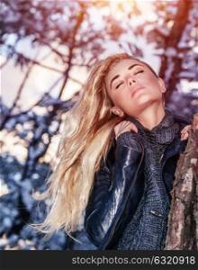 Portrait of gentle sexy blond woman with closed eyes near tree, gorgeous fashion model posing in winter park
