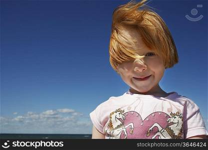 Portrait of ginger haired girl (5-6) against blue sky