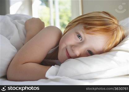 Portrait of girl (5-6) lying in bed smiling