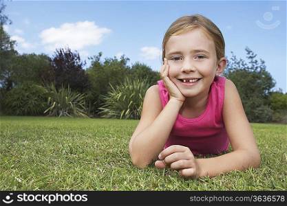 Portrait of girl (5-6) lying in grass leaning on elbow