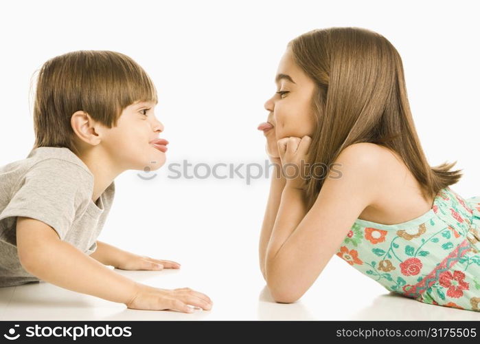 Portrait of girl and boy lying looking at eachother sticking out tongues.