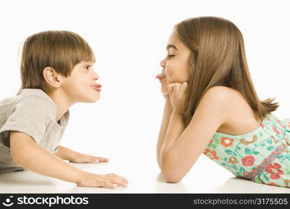 Portrait of girl and boy lying looking at eachother sticking out tongues.
