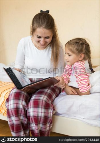 Portrait of girl and mother reading big book at bedroom