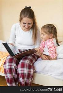 Portrait of girl and mother reading big book at bedroom