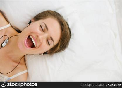 Portrait of girl in headphones laying on bed and listening music. Upper view
