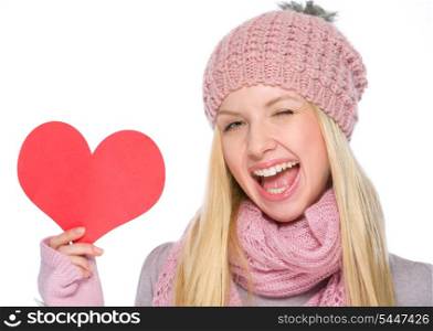 Portrait of girl in winter clothes showing heart shaped postcard and winking
