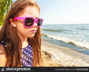 Portrait of girl outdoor in summer time.. Summer holidays and leisure. Young little girl tourist in pink sunglasses outdoors. Child waiting for parent on seaside beach.