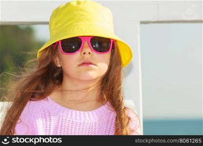 Portrait of girl outdoor in summer time.. Summer holidays and leisure. Young little girl tourist in yellow cap outdoors. Child waiting for parent on seaside beach.