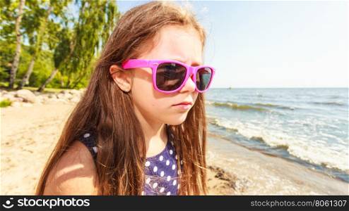 Portrait of girl outdoor in summer time.. Summer holidays and leisure. Young little girl tourist in pink sunglasses outdoors. Child waiting for parent on seaside beach.