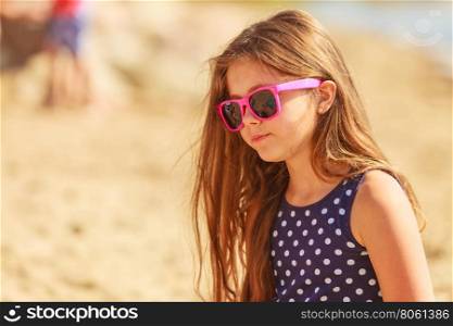 Portrait of girl outdoor in summer time.. Summer holidays and leisure. Young little girl tourist in pink sunglasses outdoors. Child waiting for parent on seaside beach.